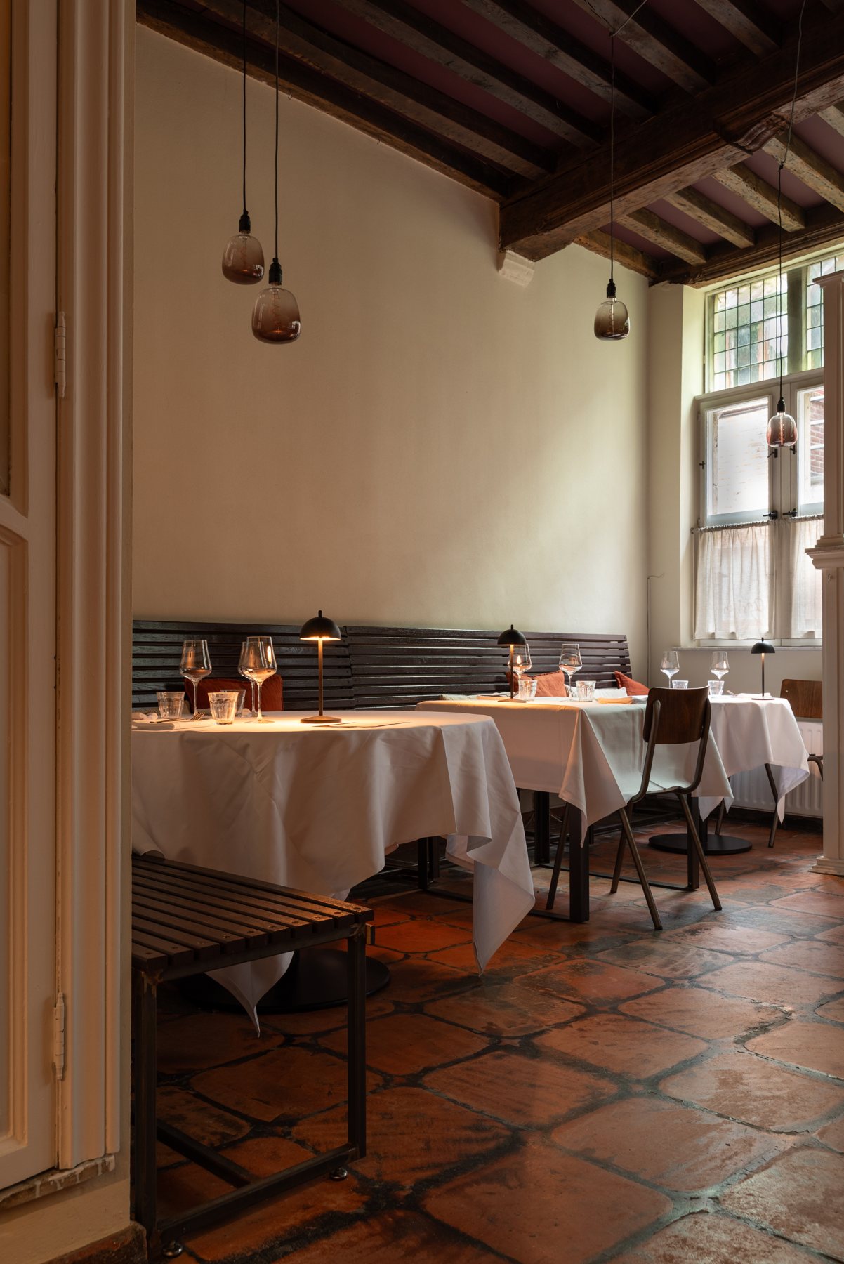 De bistrozaal met witte tafellakens, balkenplafond en terracotta vloer